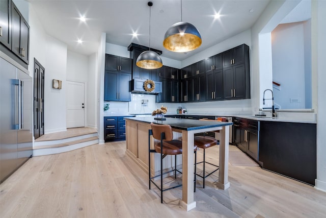 kitchen with hanging light fixtures, sink, a kitchen breakfast bar, and light hardwood / wood-style floors