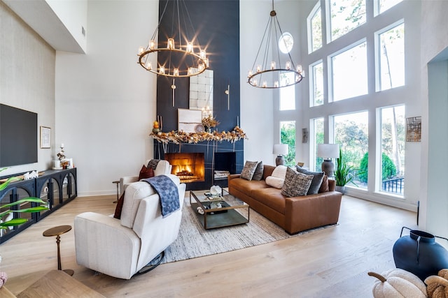 living room with a high ceiling, a tile fireplace, wood-type flooring, and an inviting chandelier