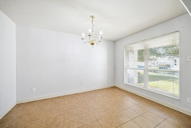 empty room featuring light tile patterned flooring, a textured ceiling, and a notable chandelier