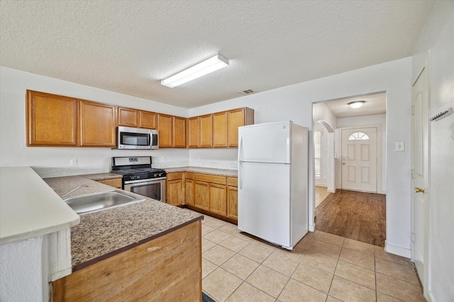 kitchen featuring appliances with stainless steel finishes, sink, a textured ceiling, and light tile patterned floors