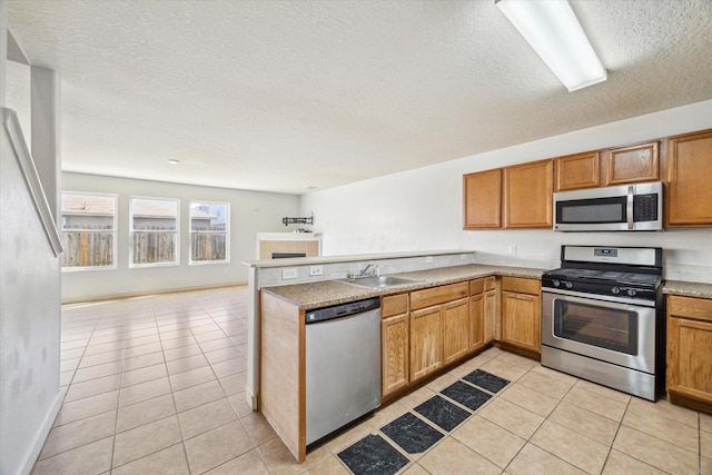 kitchen with light tile patterned flooring, stainless steel appliances, kitchen peninsula, and sink