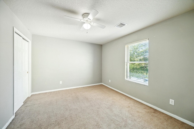 empty room featuring a textured ceiling, light colored carpet, and ceiling fan