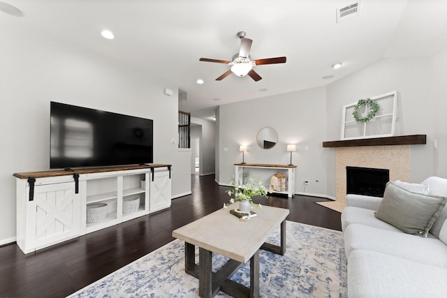 living room featuring ceiling fan, dark hardwood / wood-style floors, a tiled fireplace, and vaulted ceiling