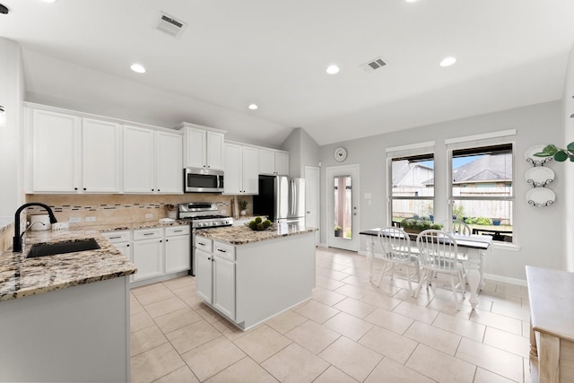 kitchen featuring sink, white cabinetry, light stone counters, appliances with stainless steel finishes, and a kitchen island