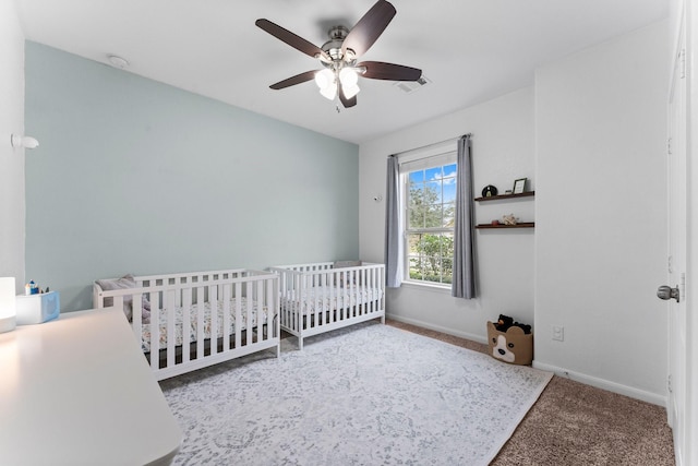 carpeted bedroom featuring a nursery area and ceiling fan