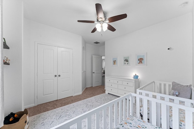 bedroom featuring a nursery area, ceiling fan, light colored carpet, and a closet