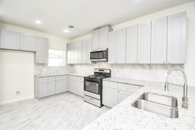 kitchen with light stone counters, sink, tasteful backsplash, and appliances with stainless steel finishes