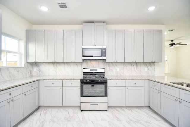 kitchen with decorative backsplash, ceiling fan, kitchen peninsula, stainless steel appliances, and light stone countertops