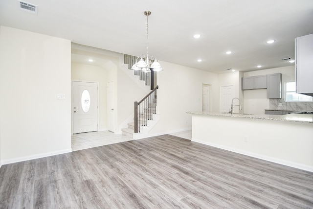 unfurnished living room featuring an inviting chandelier, sink, and light wood-type flooring