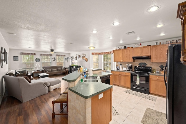 kitchen featuring sink, a kitchen island with sink, black appliances, a textured ceiling, and a kitchen bar