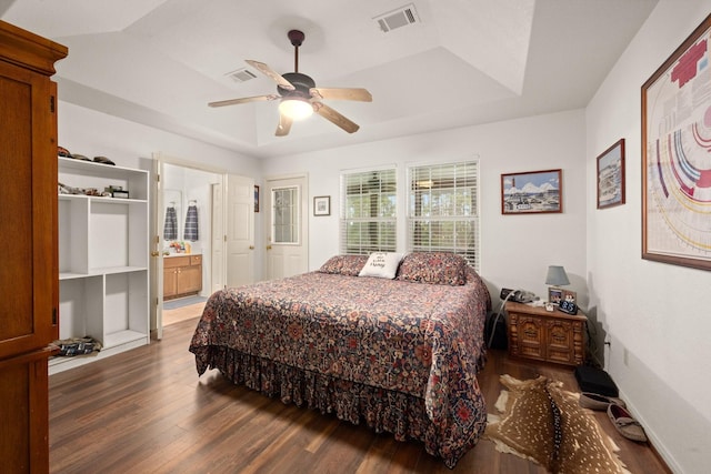 bedroom with a raised ceiling, dark wood-type flooring, ceiling fan, and ensuite bath