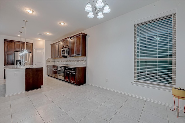 kitchen with a kitchen island with sink, stainless steel appliances, tasteful backsplash, light tile patterned flooring, and decorative light fixtures