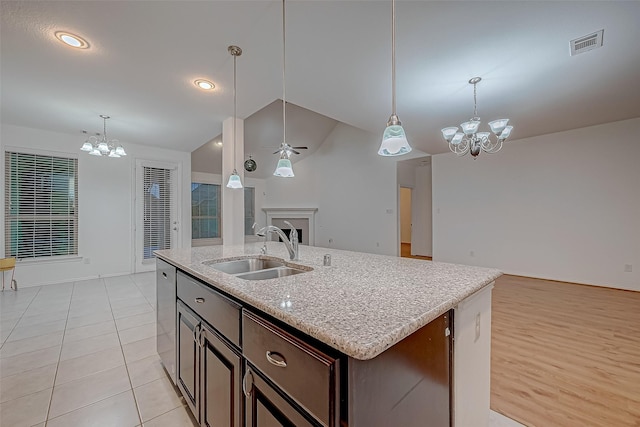 kitchen with dark brown cabinetry, a kitchen island with sink, sink, and hanging light fixtures