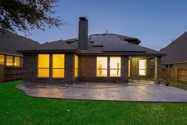 back house at dusk featuring a yard, a patio, and solar panels