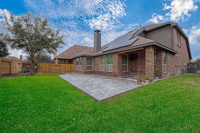 rear view of house featuring a lawn, a patio, cooling unit, and solar panels