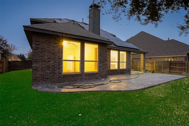 back house at dusk with a lawn, a patio, and solar panels