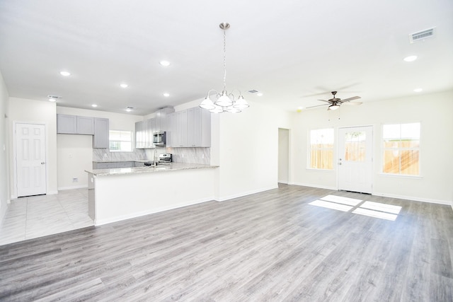 unfurnished living room featuring ceiling fan with notable chandelier and light wood-type flooring