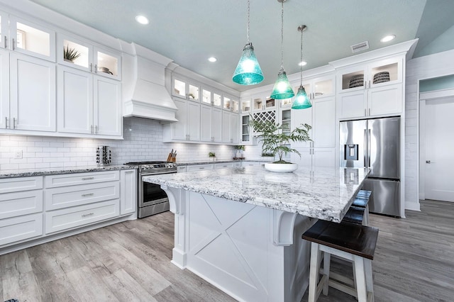 kitchen featuring decorative light fixtures, appliances with stainless steel finishes, a kitchen island, custom range hood, and white cabinets