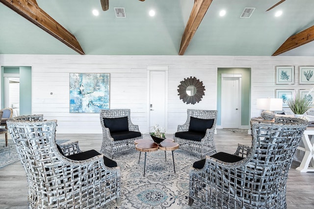 living room featuring hardwood / wood-style flooring, ceiling fan, vaulted ceiling with beams, and wooden walls