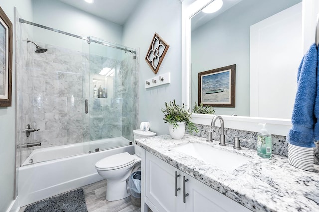 full bathroom with vanity, hardwood / wood-style flooring, bath / shower combo with glass door, and toilet