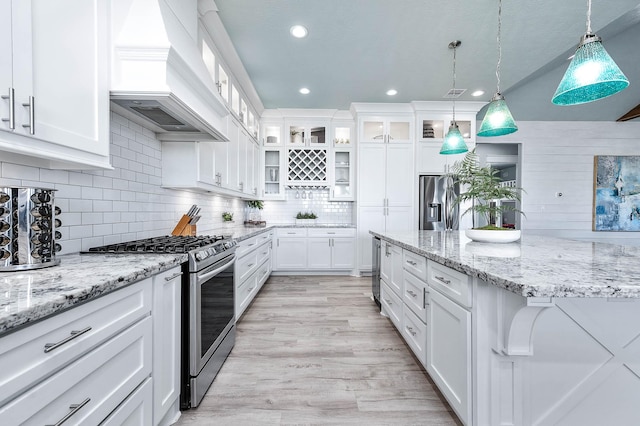 kitchen with hanging light fixtures, stainless steel range with gas stovetop, custom range hood, light hardwood / wood-style floors, and white cabinets