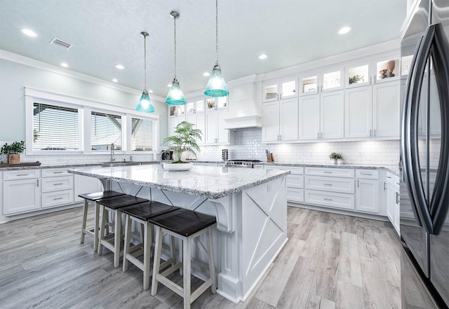 kitchen featuring premium range hood, refrigerator, white cabinets, a center island, and light stone counters