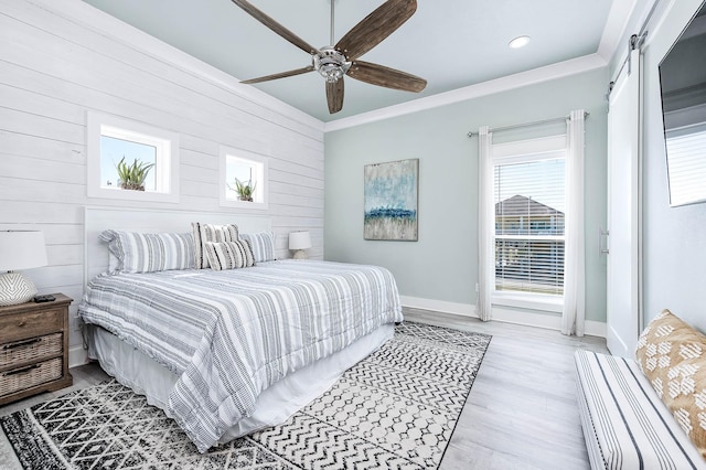 bedroom featuring crown molding, ceiling fan, wooden walls, a barn door, and light wood-type flooring