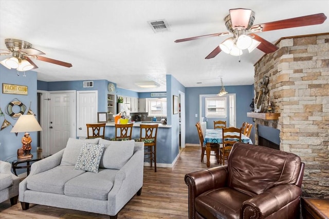 living room featuring hardwood / wood-style flooring, ceiling fan, and a stone fireplace