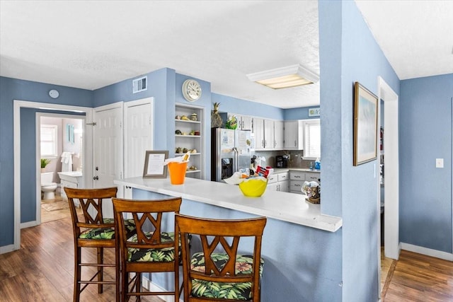 kitchen featuring a breakfast bar, white cabinetry, stainless steel fridge, kitchen peninsula, and dark hardwood / wood-style flooring