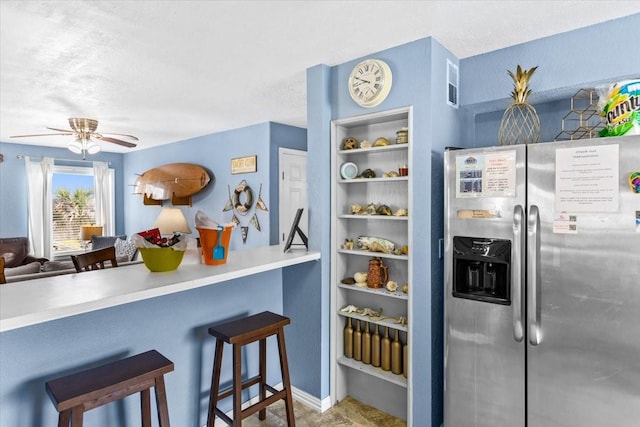 kitchen featuring stainless steel fridge with ice dispenser, a kitchen breakfast bar, ceiling fan, kitchen peninsula, and a textured ceiling