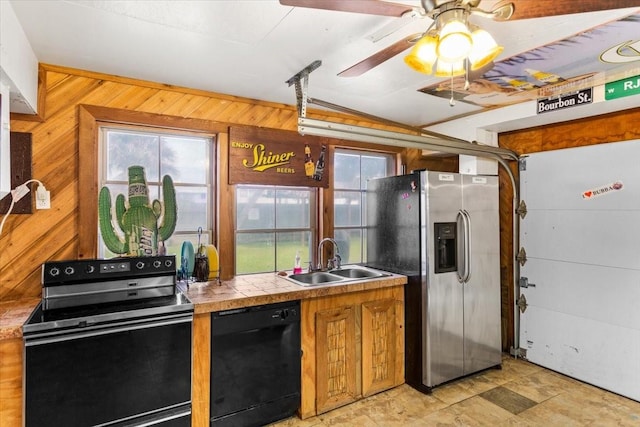 kitchen with sink, tile counters, wood walls, and black appliances