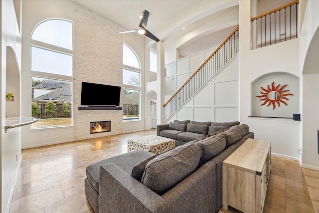 living room with a stone fireplace, a towering ceiling, and ceiling fan