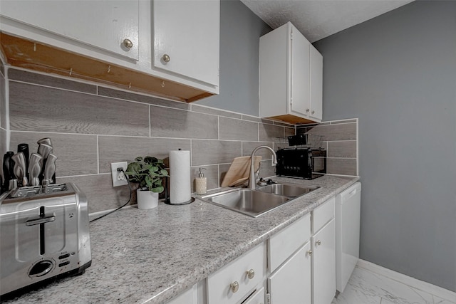 kitchen featuring white dishwasher, sink, backsplash, and white cabinets