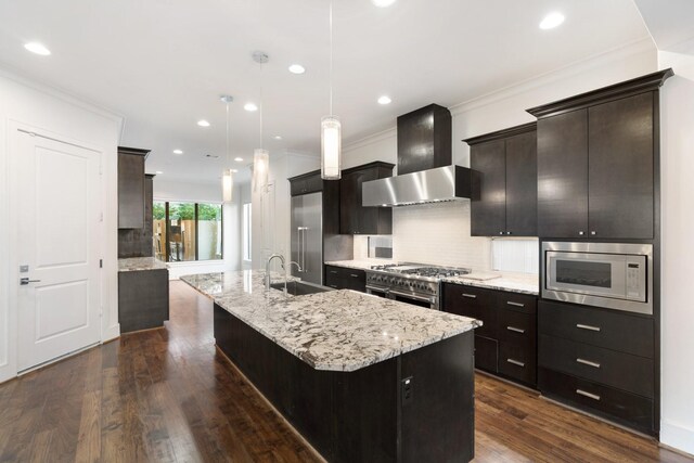 kitchen with sink, pendant lighting, stainless steel appliances, a kitchen island with sink, and wall chimney range hood