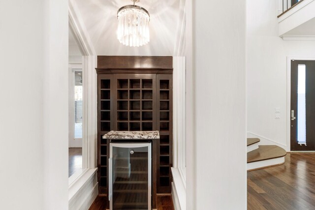 wine cellar with bar, a notable chandelier, dark wood-type flooring, and beverage cooler