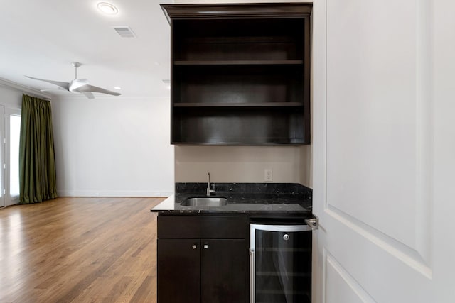 bar featuring wine cooler, dark brown cabinetry, sink, light hardwood / wood-style flooring, and dark stone countertops