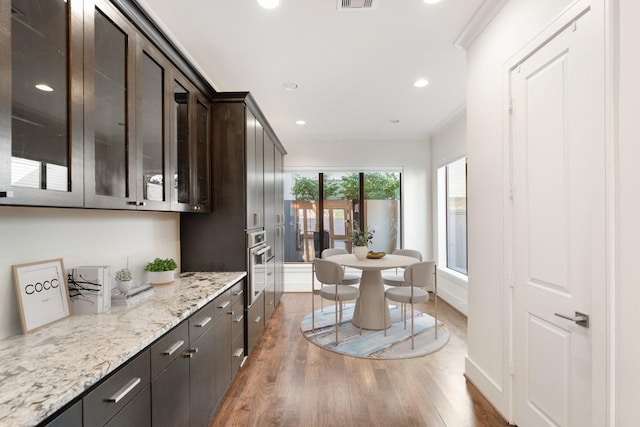 kitchen with crown molding, dark brown cabinets, dark hardwood / wood-style floors, light stone countertops, and oven