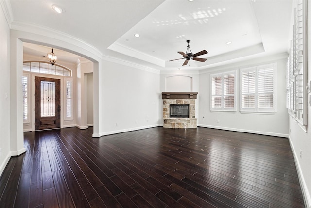 unfurnished living room with a tray ceiling, a stone fireplace, ornamental molding, and dark hardwood / wood-style floors