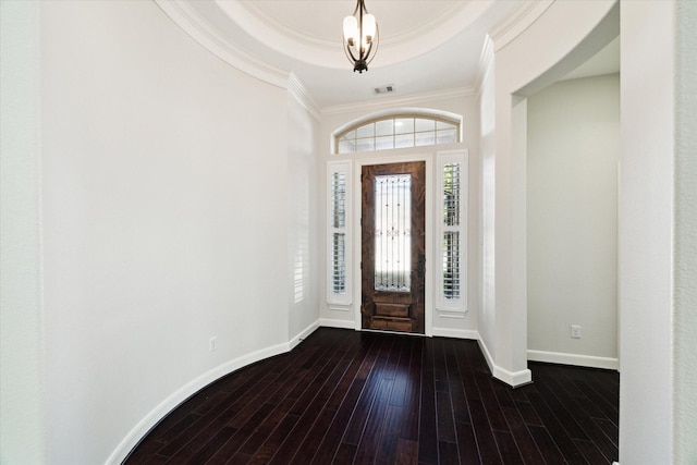 entryway with crown molding, dark hardwood / wood-style floors, a raised ceiling, and a notable chandelier