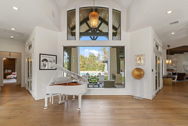 entryway with high vaulted ceiling, a textured ceiling, a chandelier, and light hardwood / wood-style flooring