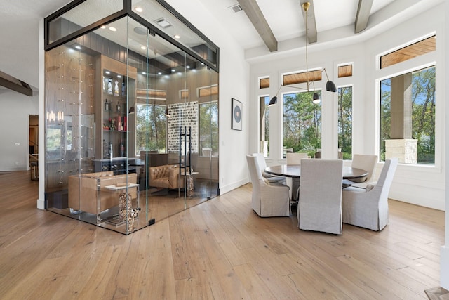 dining space featuring beam ceiling, light hardwood / wood-style flooring, and a high ceiling