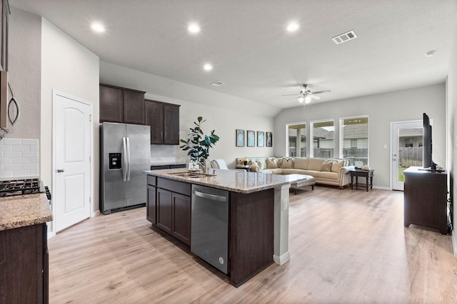 kitchen with a kitchen island with sink, backsplash, dark brown cabinets, stainless steel appliances, and vaulted ceiling