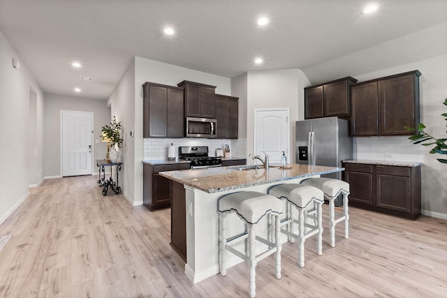 kitchen with sink, a kitchen breakfast bar, an island with sink, stainless steel appliances, and light stone countertops