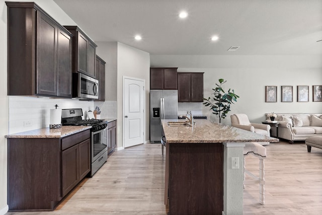 kitchen featuring sink, appliances with stainless steel finishes, a kitchen island with sink, backsplash, and a kitchen breakfast bar