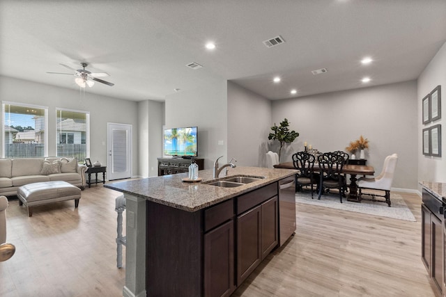 kitchen featuring dishwasher, an island with sink, sink, light stone countertops, and light hardwood / wood-style flooring