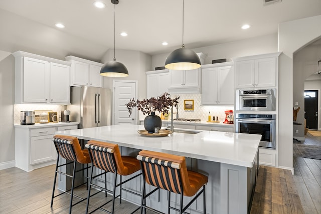 kitchen featuring a kitchen bar, stainless steel appliances, white cabinets, and a center island with sink