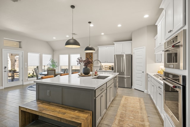 kitchen with pendant lighting, sink, appliances with stainless steel finishes, a kitchen island with sink, and white cabinets