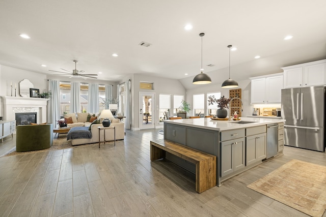 kitchen with appliances with stainless steel finishes, white cabinetry, an island with sink, gray cabinetry, and hanging light fixtures