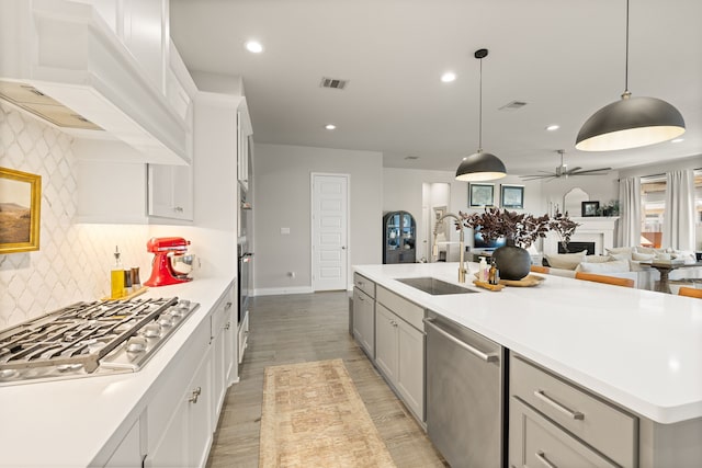 kitchen featuring appliances with stainless steel finishes, decorative light fixtures, sink, custom range hood, and a center island with sink