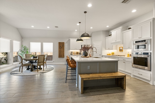 kitchen with pendant lighting, sink, white cabinetry, a kitchen island with sink, and light hardwood / wood-style floors